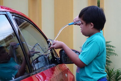 Side view of boy washing eyeglasses while standing by car