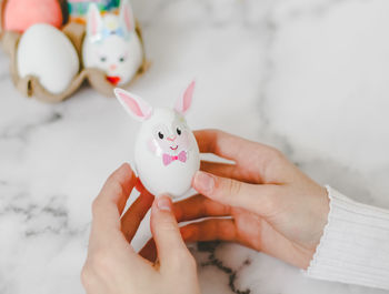 Hands of a caucasian girl holding a white easter bunny egg made by her own hands,