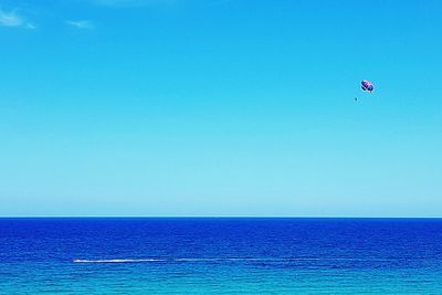 Person paragliding in sea against clear blue sky