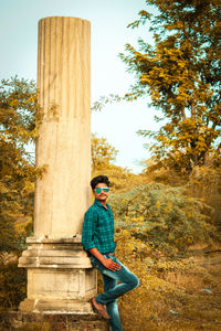 Portrait of young man standing bu column in forest