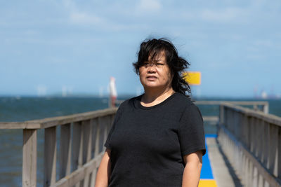 Portrait of teenage girl standing on railing against sea