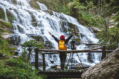 Rear view of woman with camera enjoying waterfall view in forest