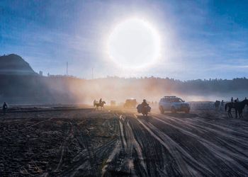 Panoramic view of desert people on field against sun sky