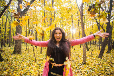 Happy young woman with arms outstretched standing on autumn leaves