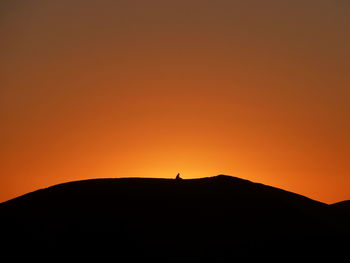 Silhouette person standing on mountain against orange sky