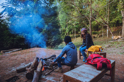 Rear view of people sitting on bench in forest