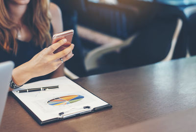 Midsection of woman using smart phone on table