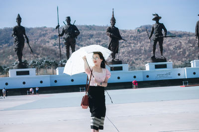 Young woman with umbrella standing on road against statues