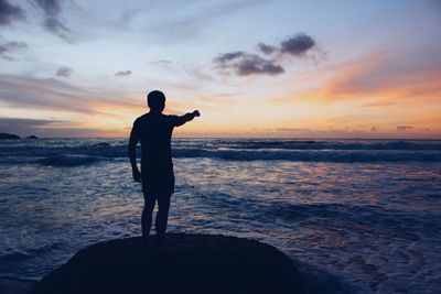 Silhouette man standing on rock at beach during sunset