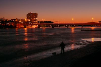 Silhouette man standing by illuminated cityscape against sky during sunset