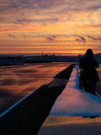 Rear view of woman standing on bridge against sky during sunset