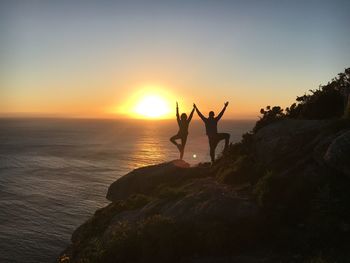 Silhouette people standing on rock by sea against sky during sunset