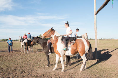 Men riding horses on field against sky