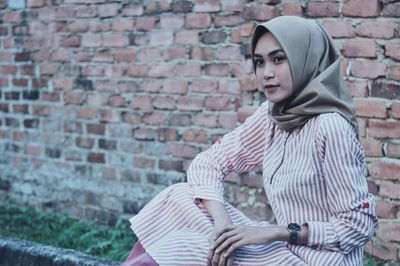 Portrait of young woman standing against brick wall