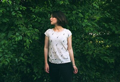 Woman looking away while standing against plants