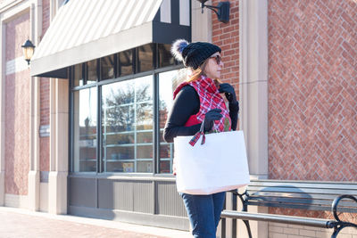 Woman holding shopping bag while standing against building in city