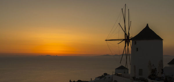 Silhouette traditional windmill by sea against sky during sunset