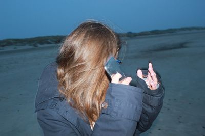Woman hiding face with mobile phone at beach