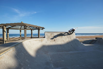 Unrecognizable teen boy in riding skateboard in skate park on sunny day on seashore