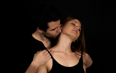 Man kissing woman on neck against black background