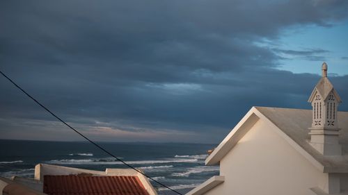 Buildings by sea against storm clouds