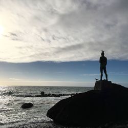 Silhouette man standing on rock by sea against sky