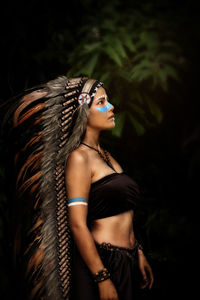 Side view of young woman in costume looking away against trees at night