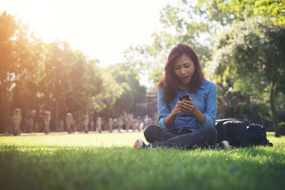 Young woman using smart phone while sitting on grassy field