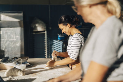 Smiling female baker kneading dough with senior colleague while working at bakery