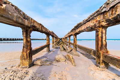 Abandoned pier on beach against sky