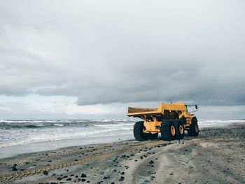 Yellow truck at beach against cloudy sky