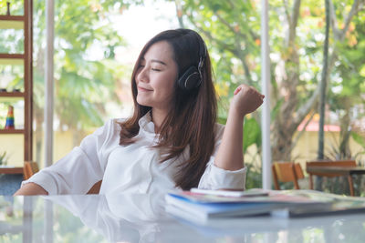 Smiling woman listening music through headphones while sitting at restaurant table