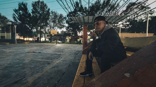 Side view of young man sitting on tree