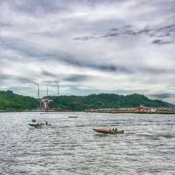 Boats in sea against cloudy sky