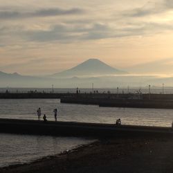 Silhouette people on beach against cloudy sky