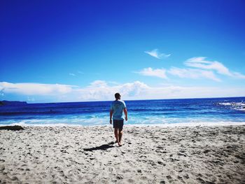 Rear view of woman standing on beach against sky