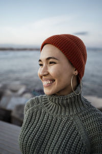 Young woman wearing knit hat smiling while standing against sky