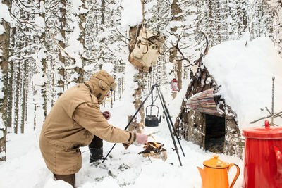 Man preparing tea in winter forest next to a wooden shelter, salzburg state, austria