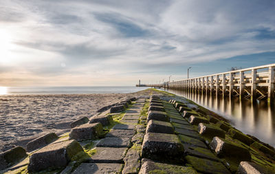 Weathered walkway by pier over sea against cloudy sky