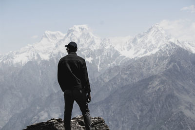 Rear view of man standing on rock against snowcapped mountains