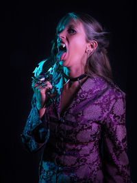 Portrait of spooky woman licking weapon against black background