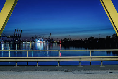 Illuminated city by river against blue sky