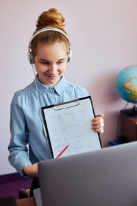 Smiling teenage girl showing homework during online lecture