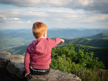 Rear view of boy looking at mountains against sky