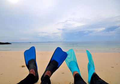 Low section of people on beach against sky