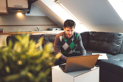 Young woman using laptop while sitting on sofa at home