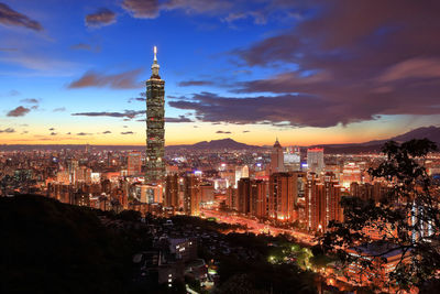 View of illuminated cityscape against cloudy sky