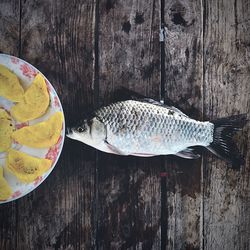 Directly above shot of fish by plate on wooden table