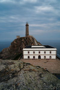 Lighthouse on rock by sea against sky