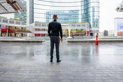 Full length rear view of man standing in city during rainy season